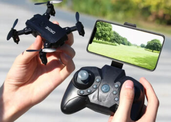 a person holding remote controller attached to a smart phone in one hand mini drone in other