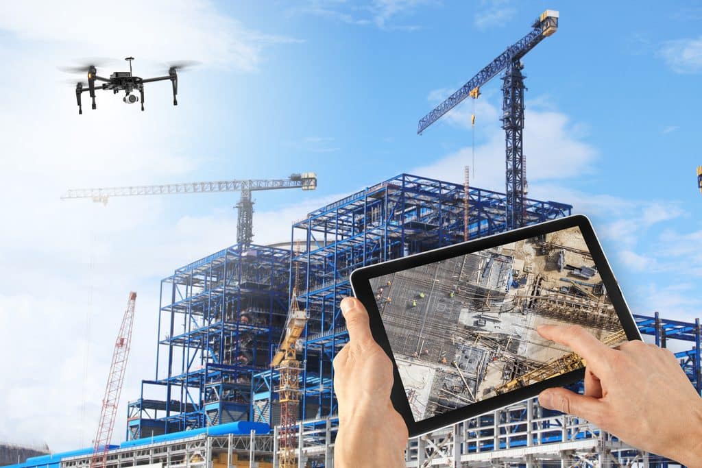 a person holding a tab and operating a drone flying above the construction area